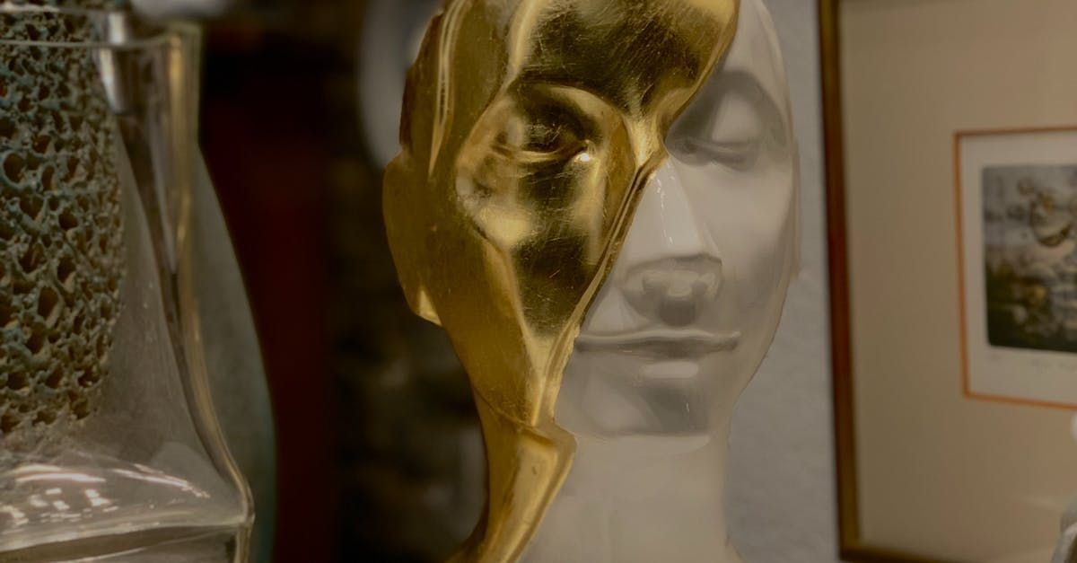 a gold statue of a man 's head is sitting on a table next to a glass vase .