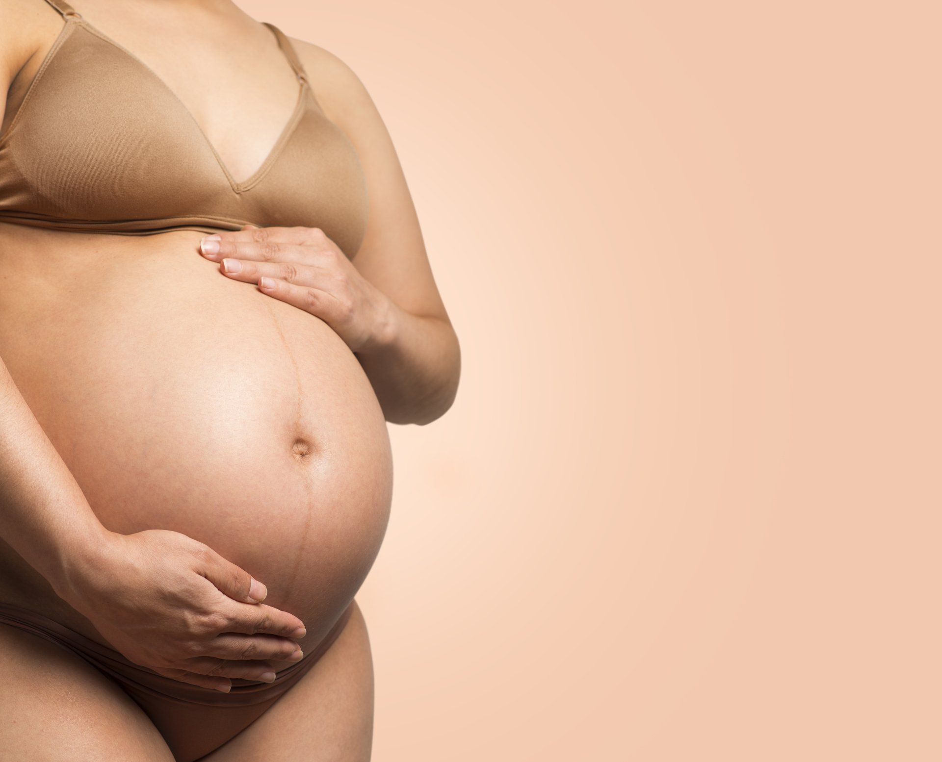 A pregnant woman in a bra is holding her belly.