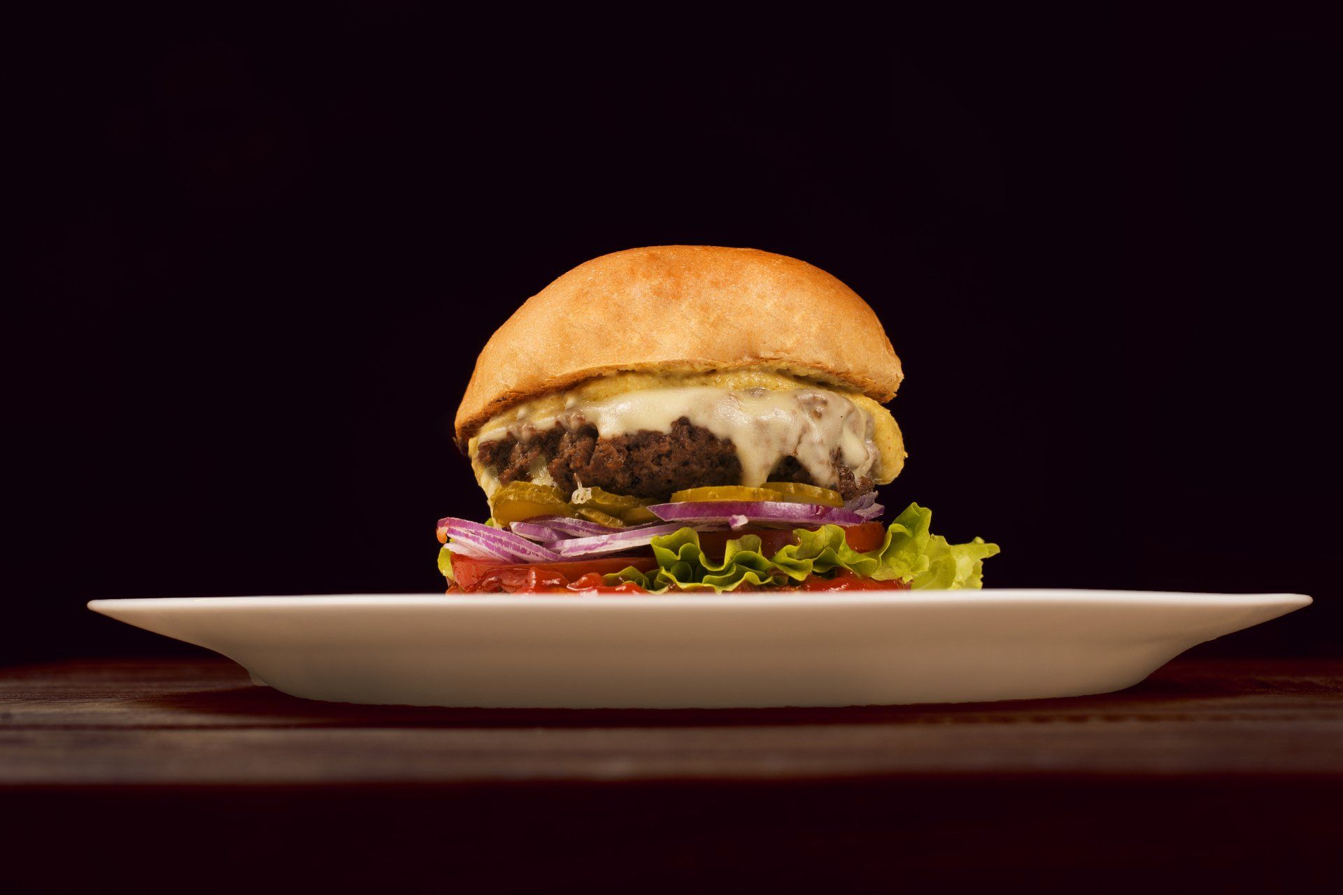 A hamburger is on a white plate on a wooden table.