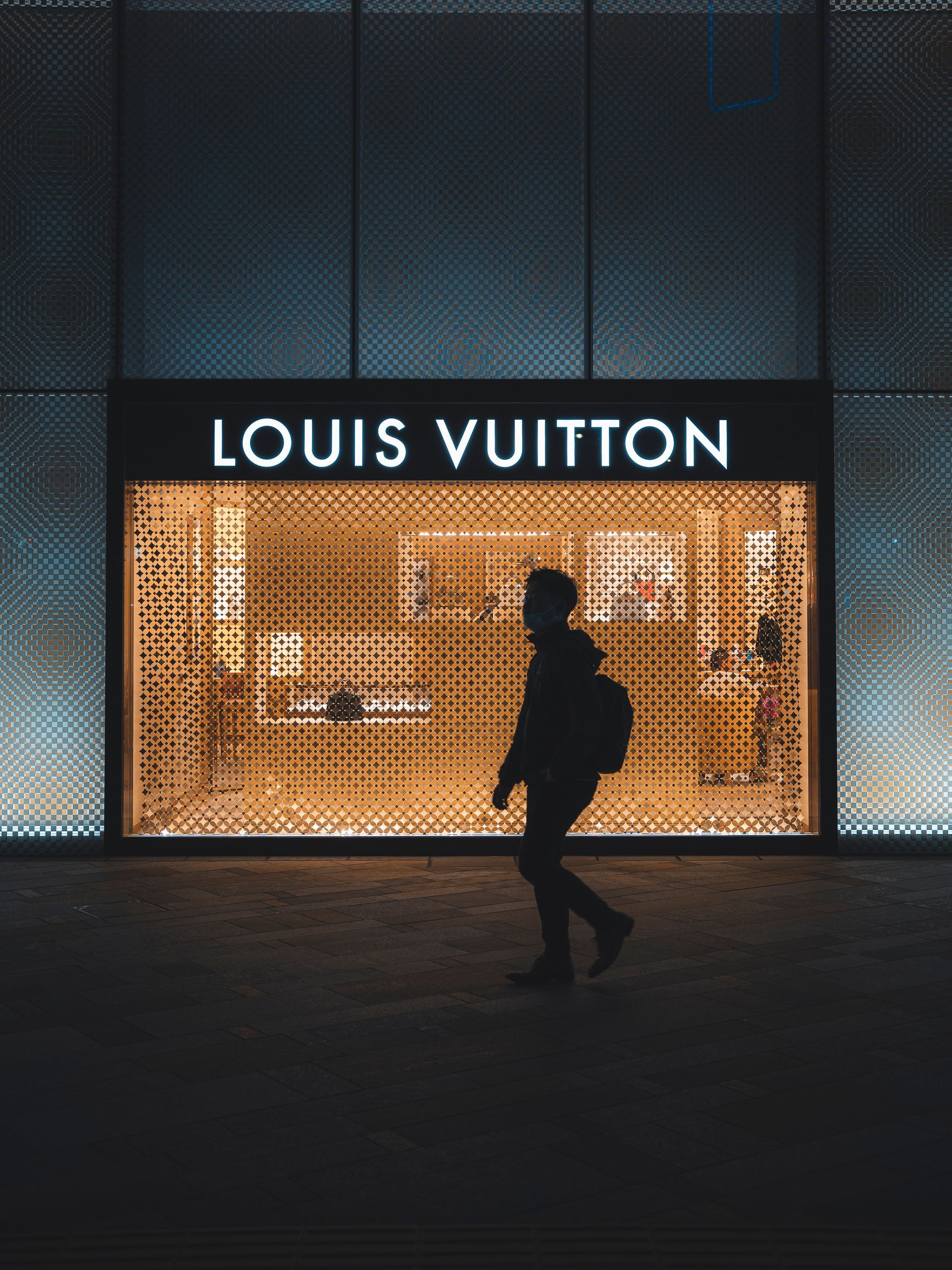 a man is walking in front of a louis vuitton store .