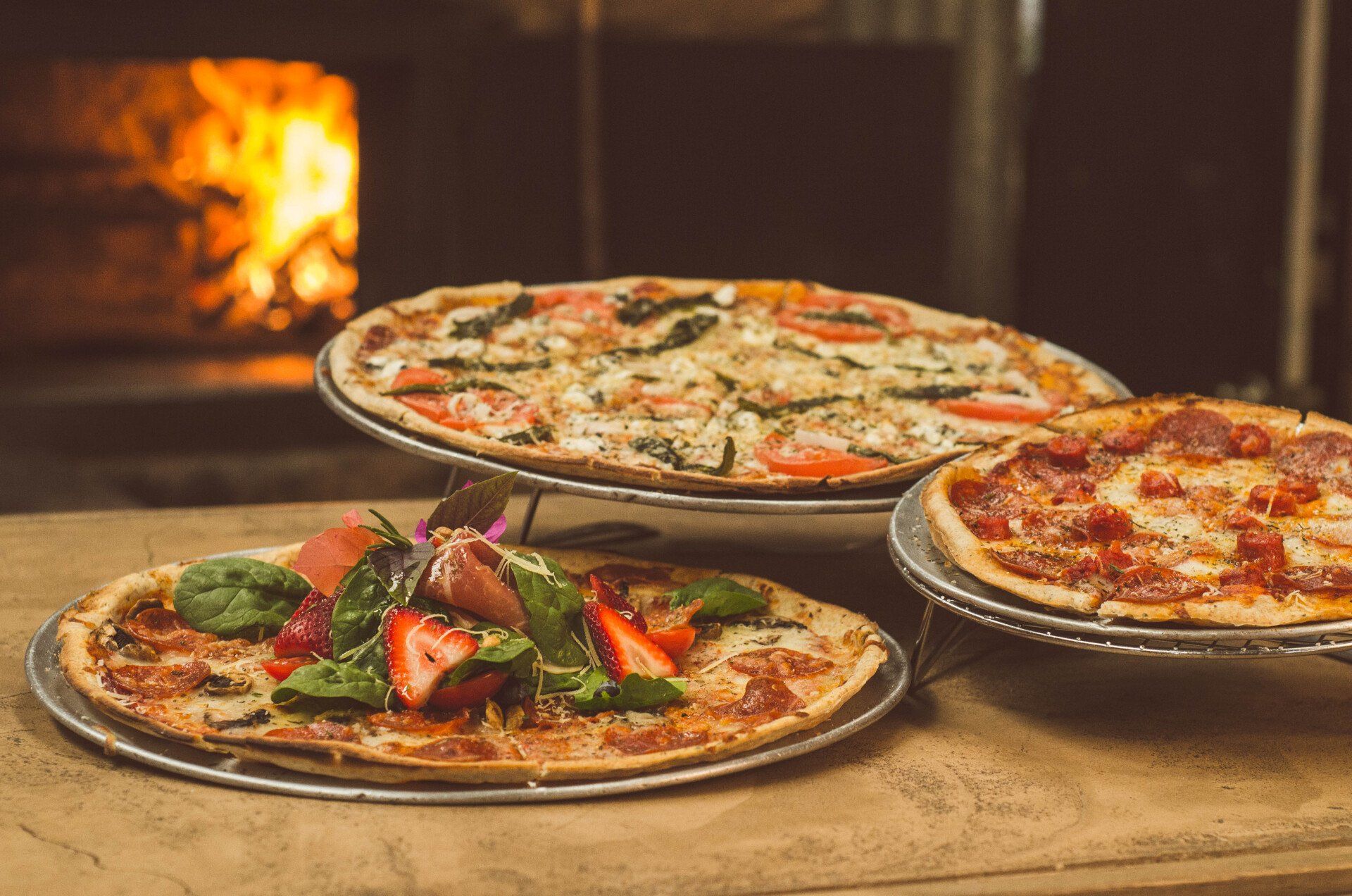 Three pizzas are stacked on top of each other on a wooden table.