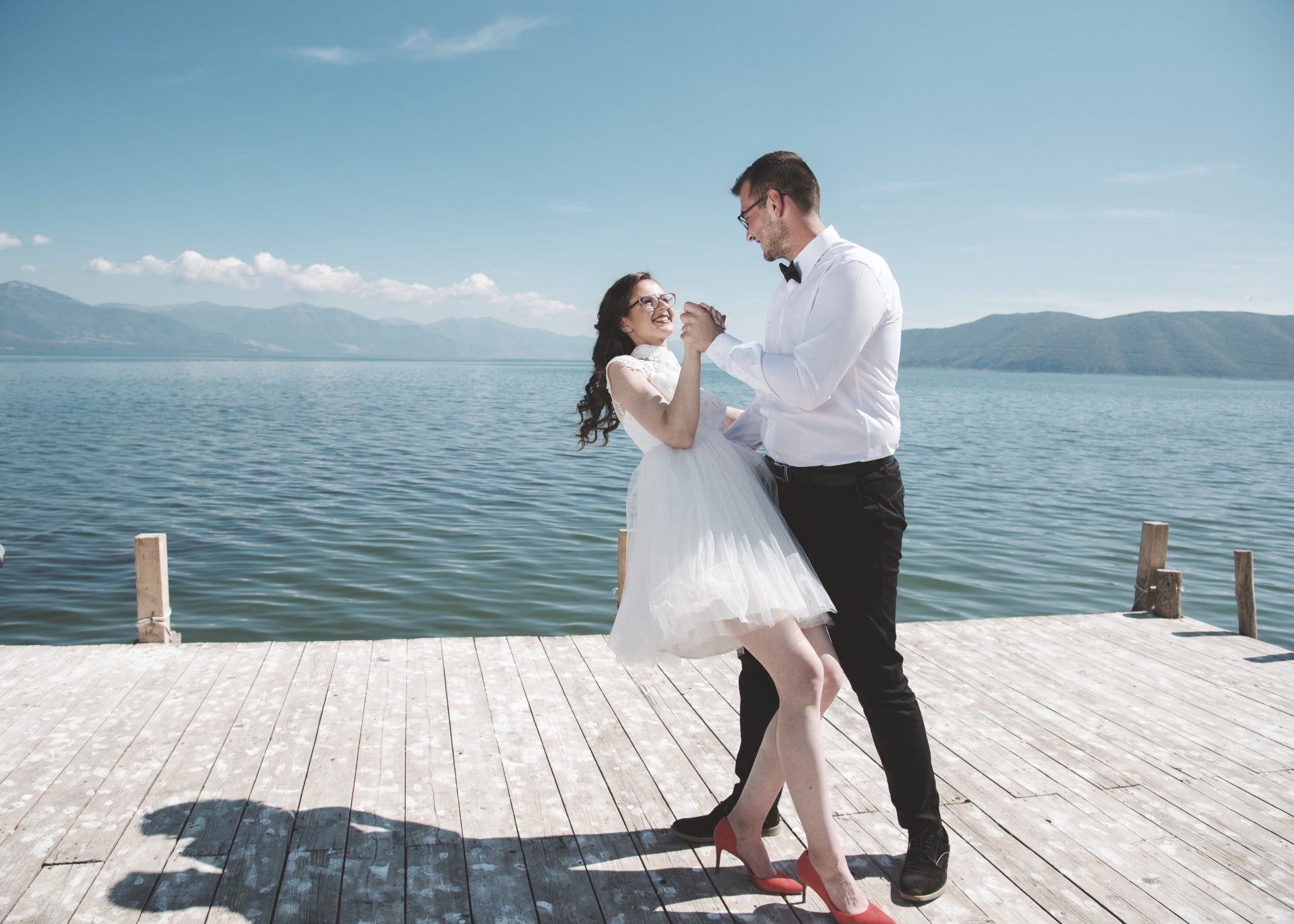 Une mariée et un marié dansent sur un quai près d'un lac.