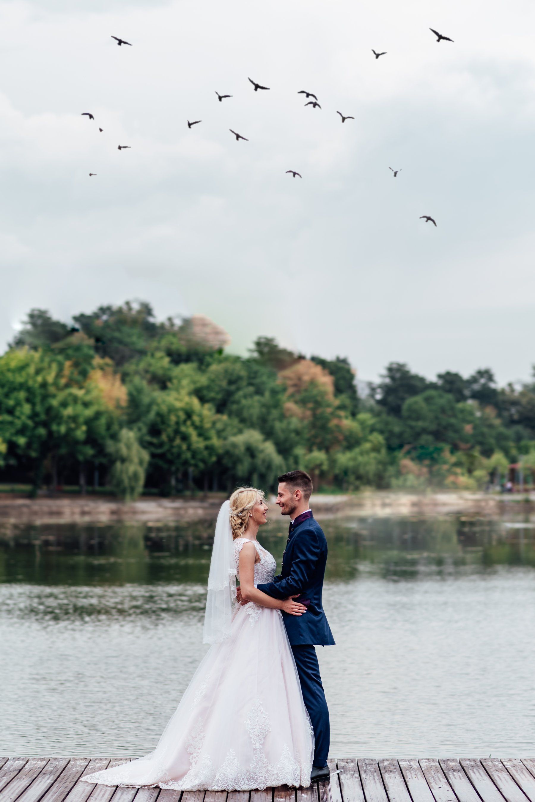 A bride and groom are standing on a dock next to a lake.