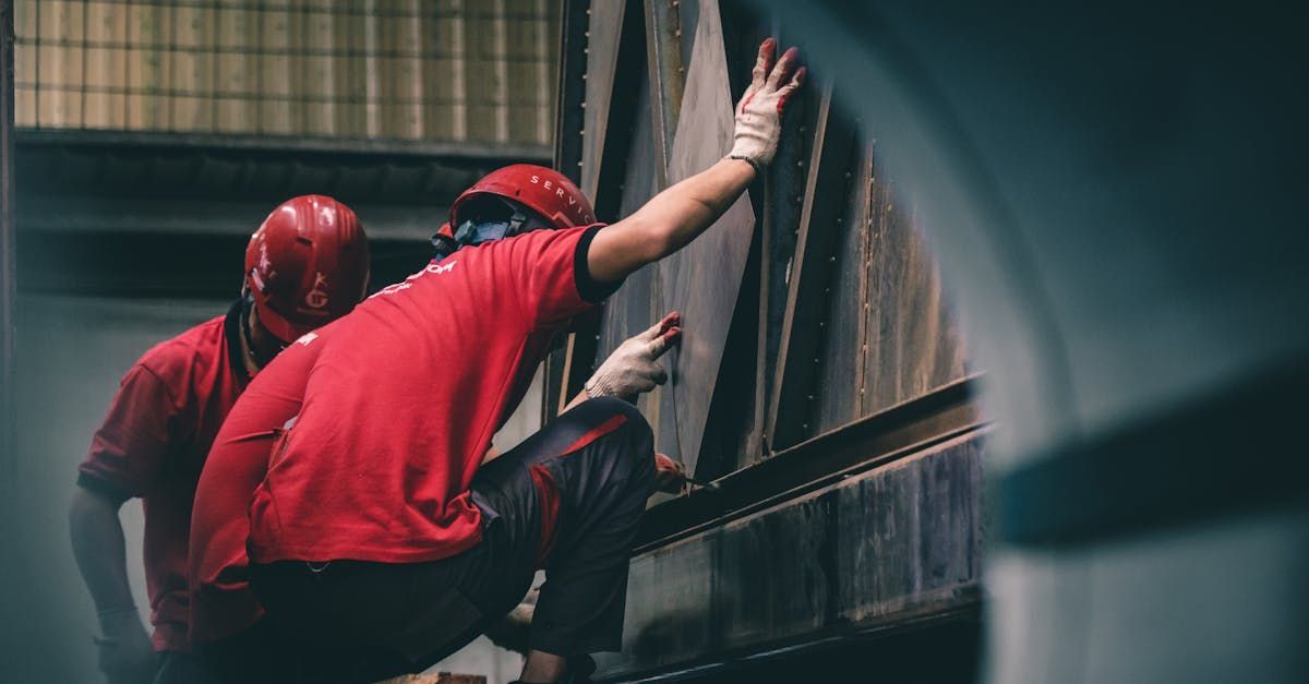 Two men in red shirts and helmets are climbing a wall.