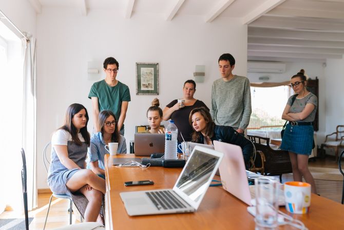 A group of people are sitting around a table with laptops.