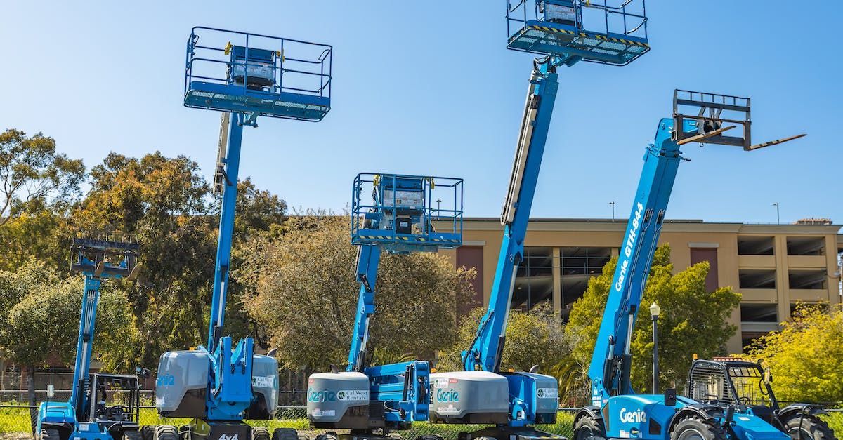 a group of aerial lifts are parked next to each other in a parking lot .