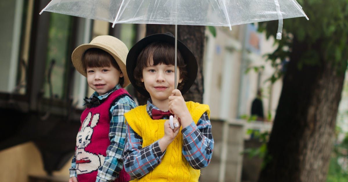Two young kids standing in the rain under an umbrella.