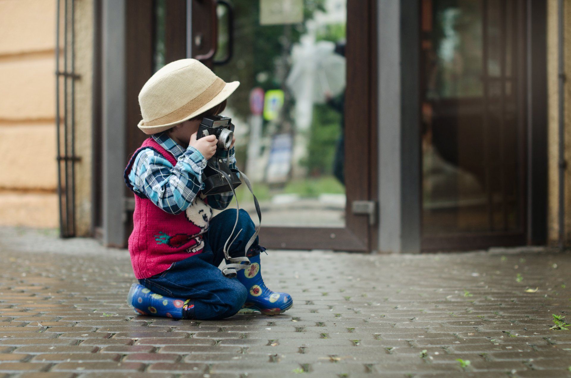 A little boy is kneeling down and taking a picture with a camera.