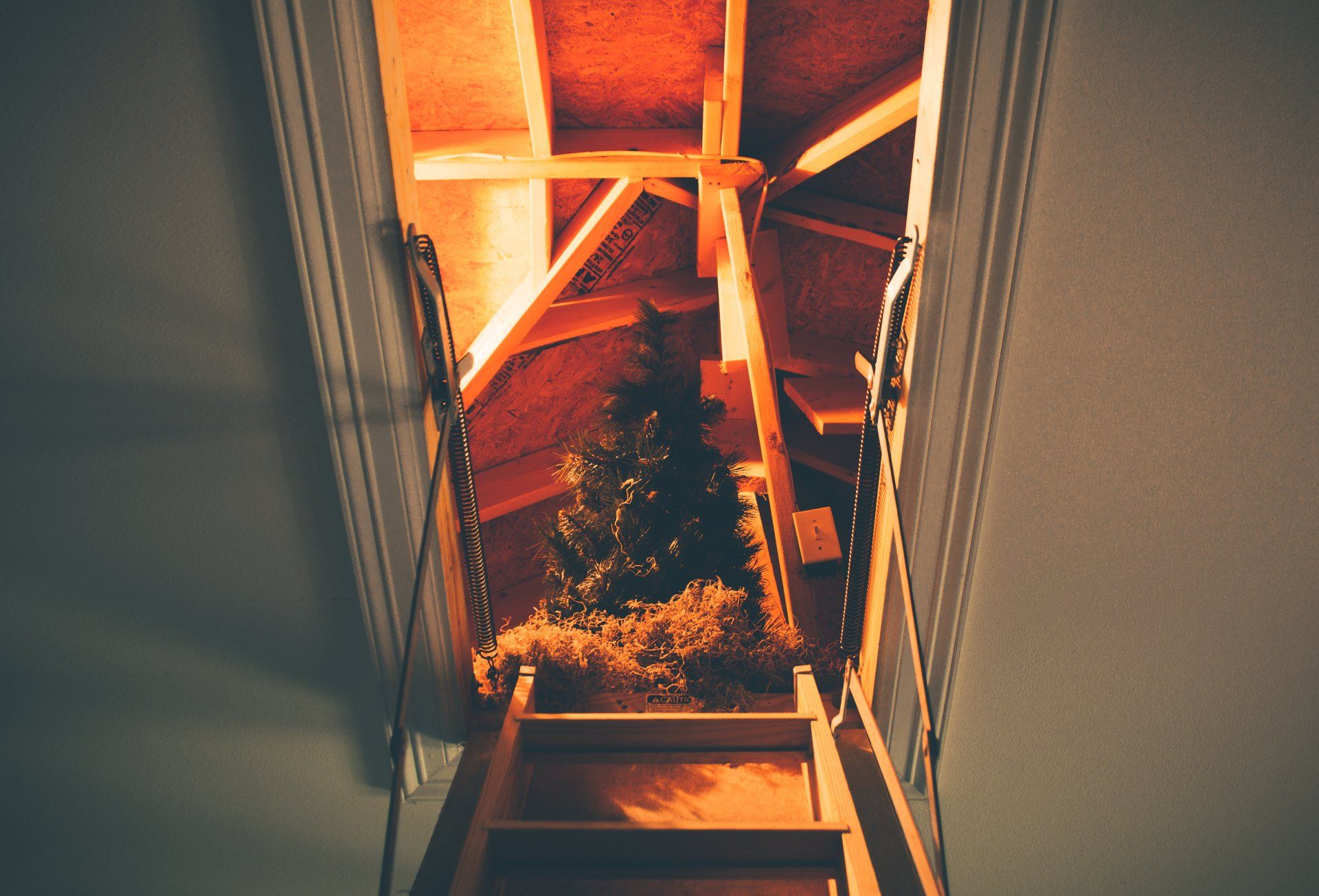 An inviting wooden staircase with a modern black metal railing, leading up to a warmly lit loft.