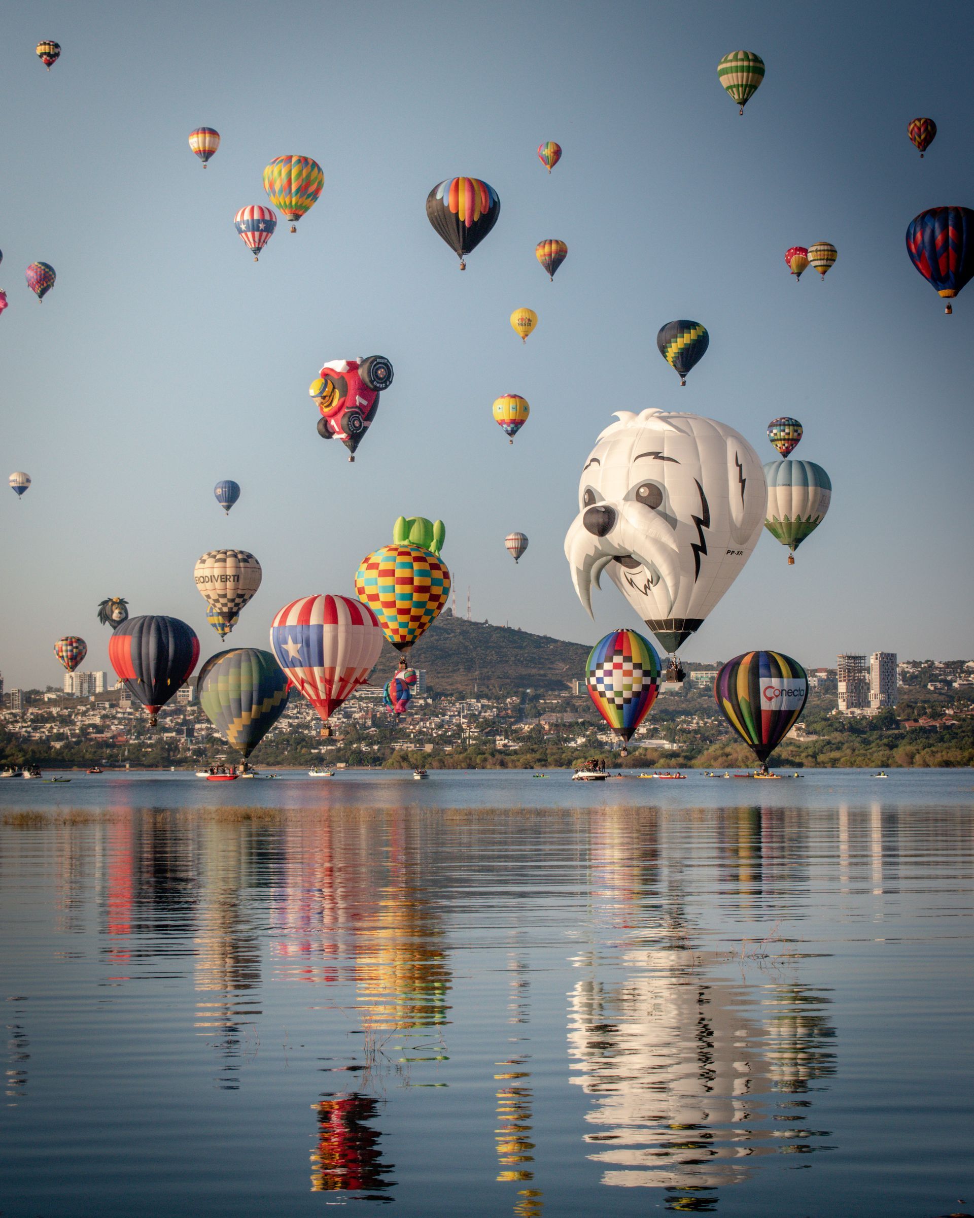 A bunch of hot air balloons are flying over a body of water.