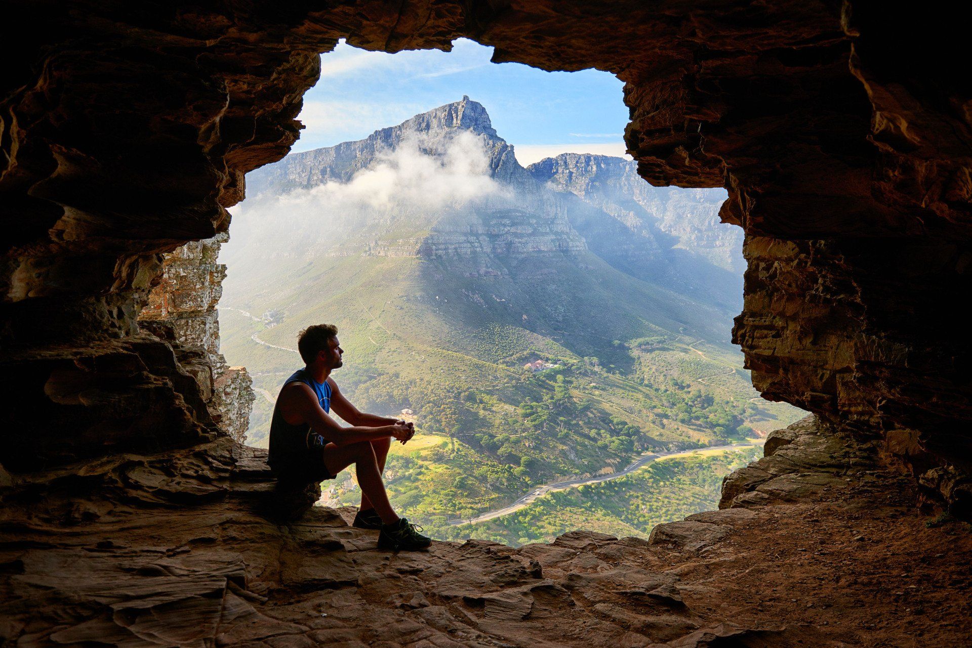 man sitting at opening of cave mountain