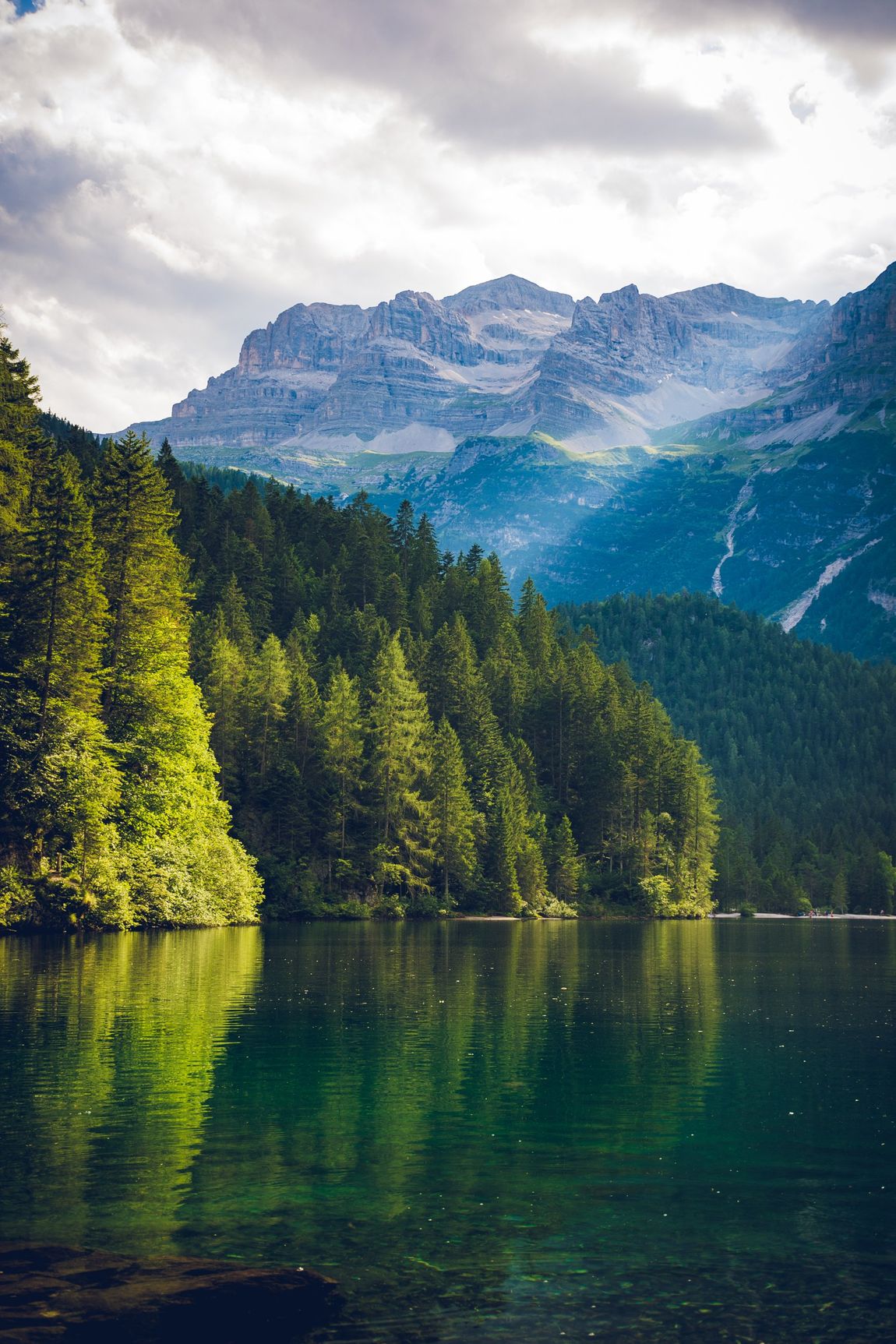 There is a lake in the middle of a forest with mountains in the background.