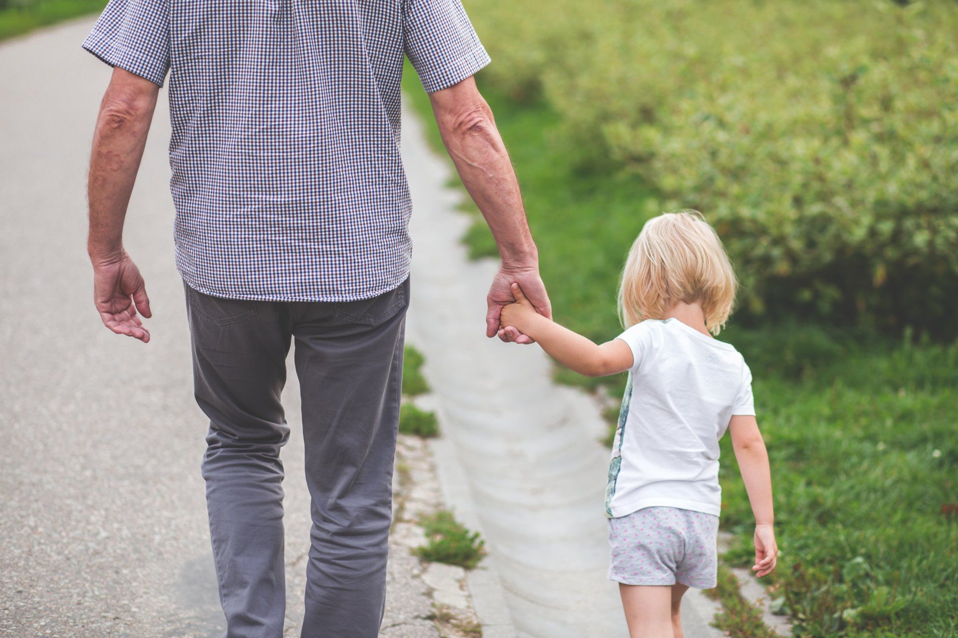 A man and a little girl are walking down a path holding hands.