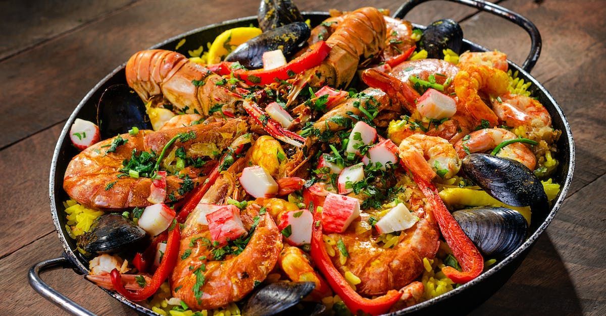 a pan filled with shrimp , mussels , peppers and rice on a wooden table .