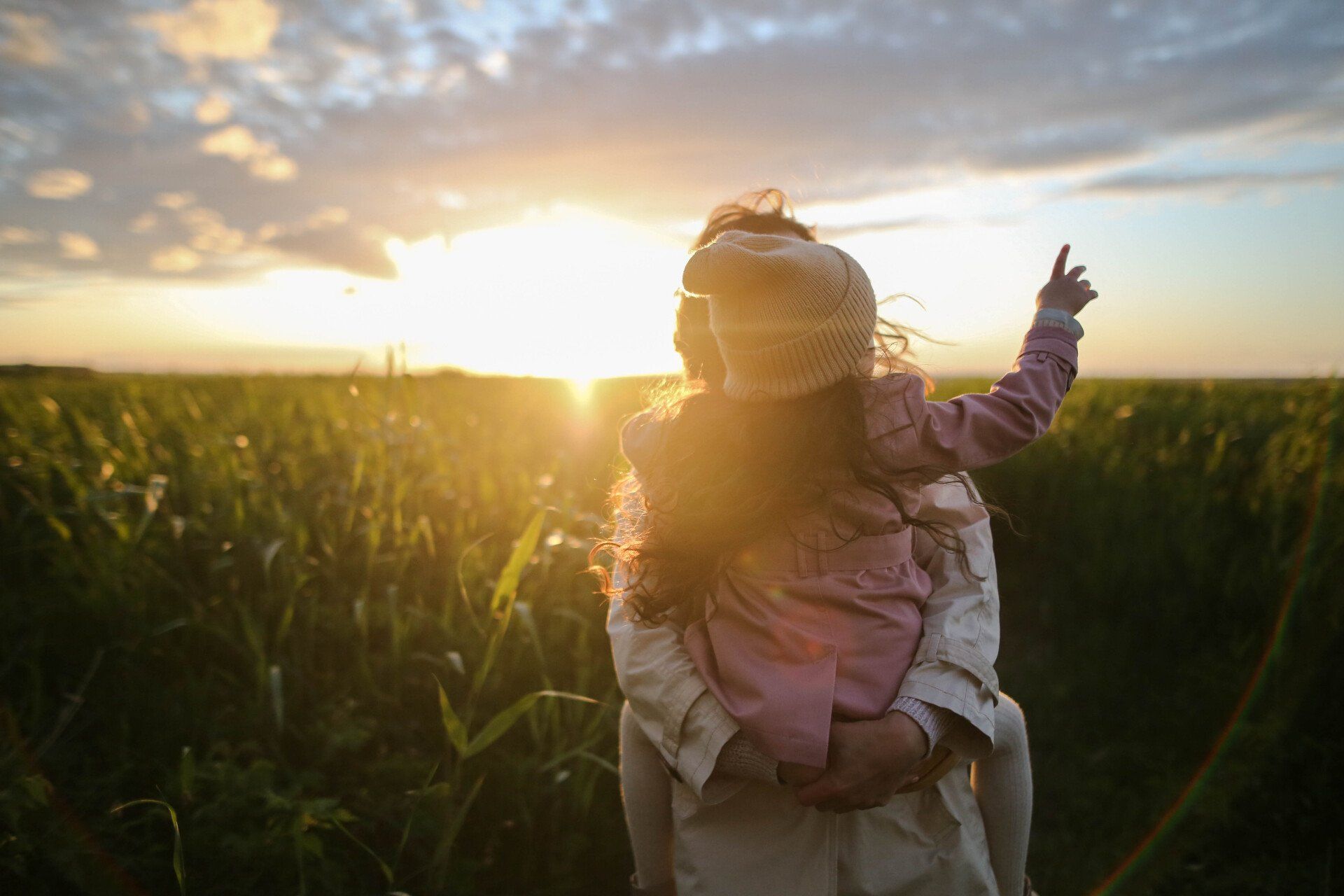 a woman is carrying a little girl on her shoulders in a field at sunset .