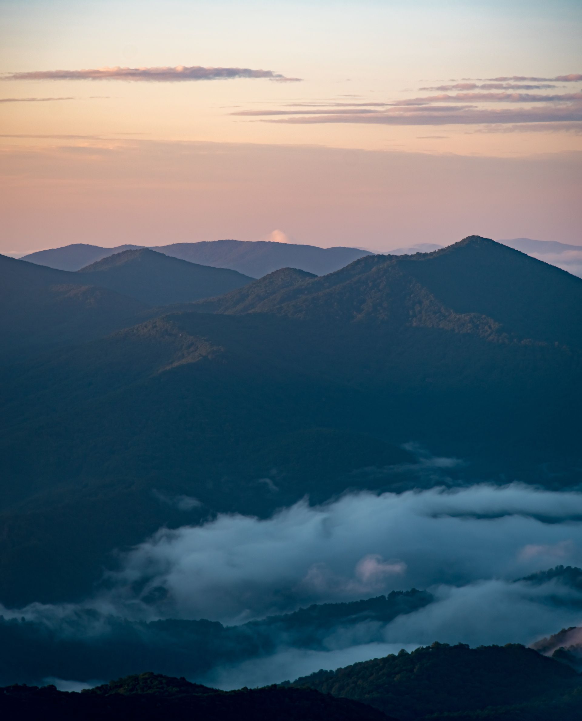 A view of a mountain range covered in clouds at sunset.