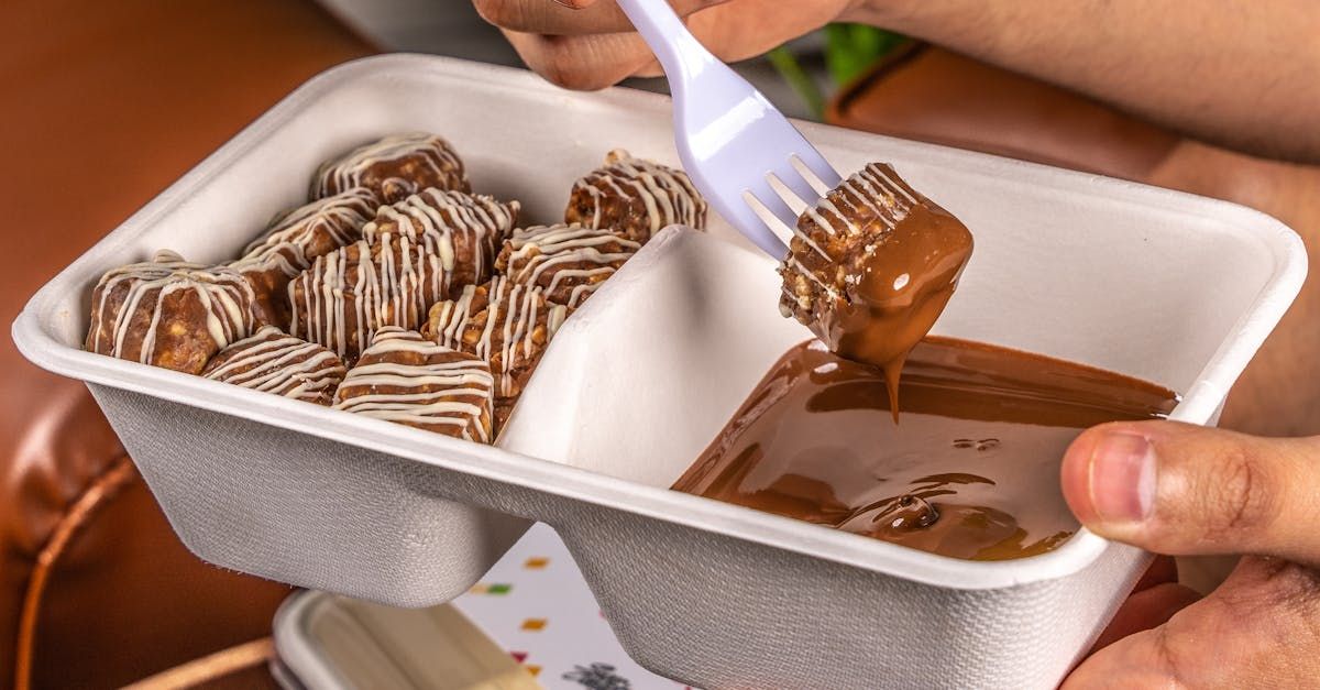 A person is dipping a piece of food in chocolate sauce with a fork.