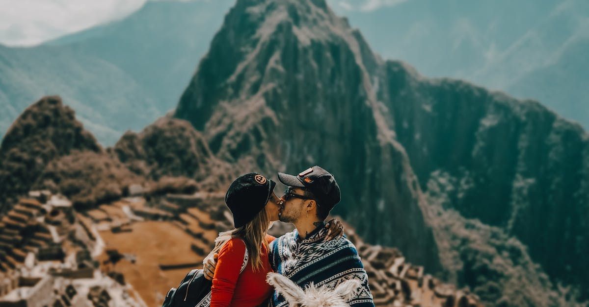 A man and a woman are kissing on top of a mountain.