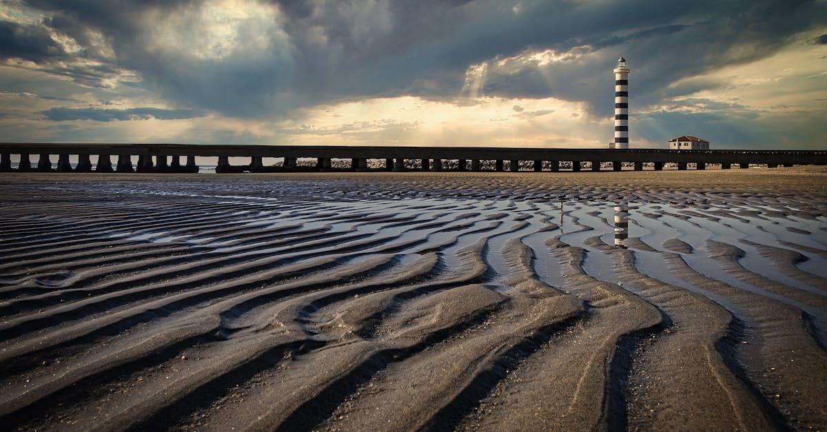 A sandy beach with a pier in the background and a lighthouse in the distance.