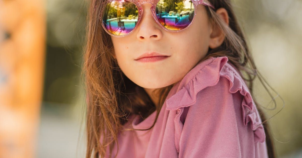 Une petite fille portant des lunettes de soleil et une chemise rose regarde la caméra.