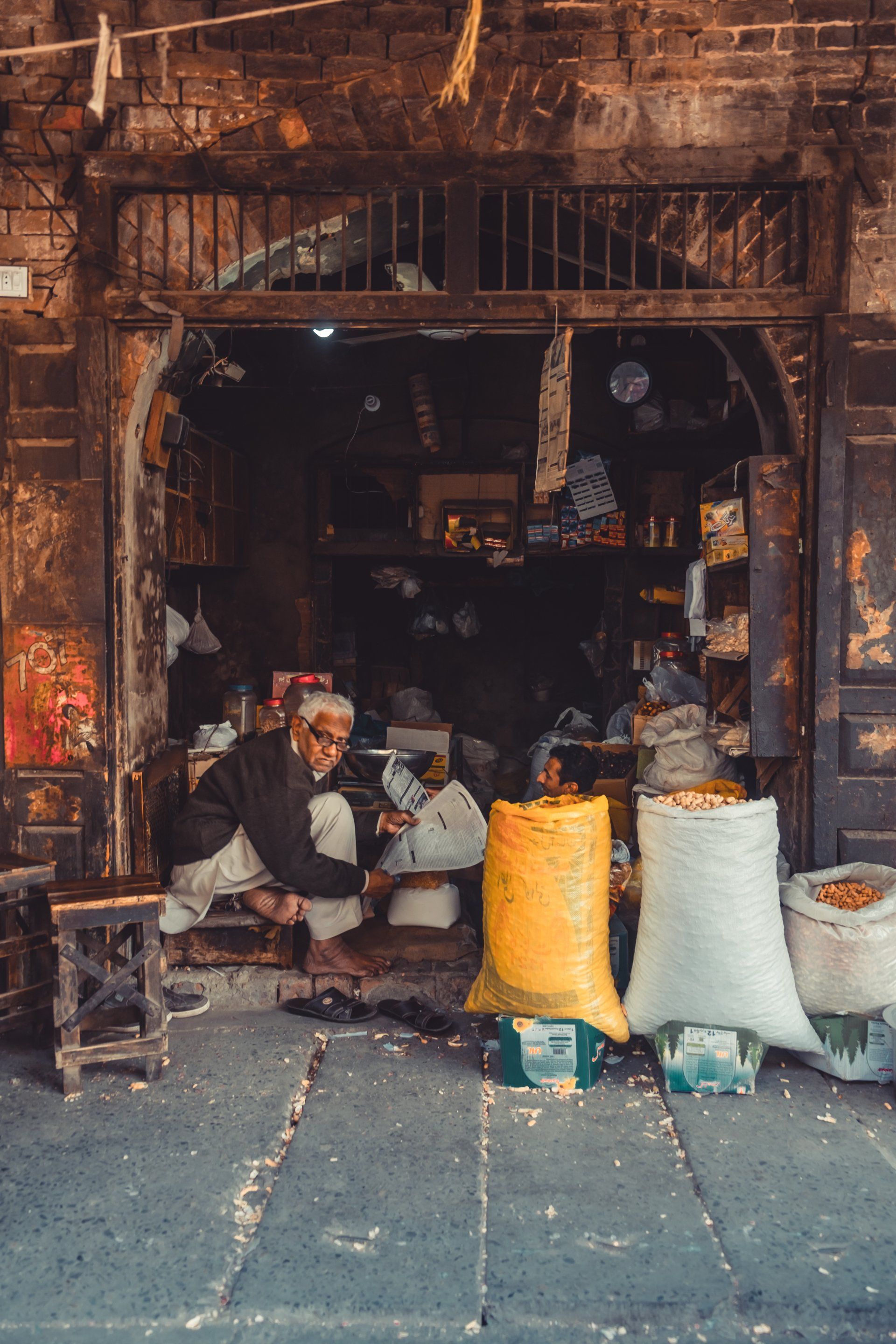A man is sitting in front of a store with bags of food.