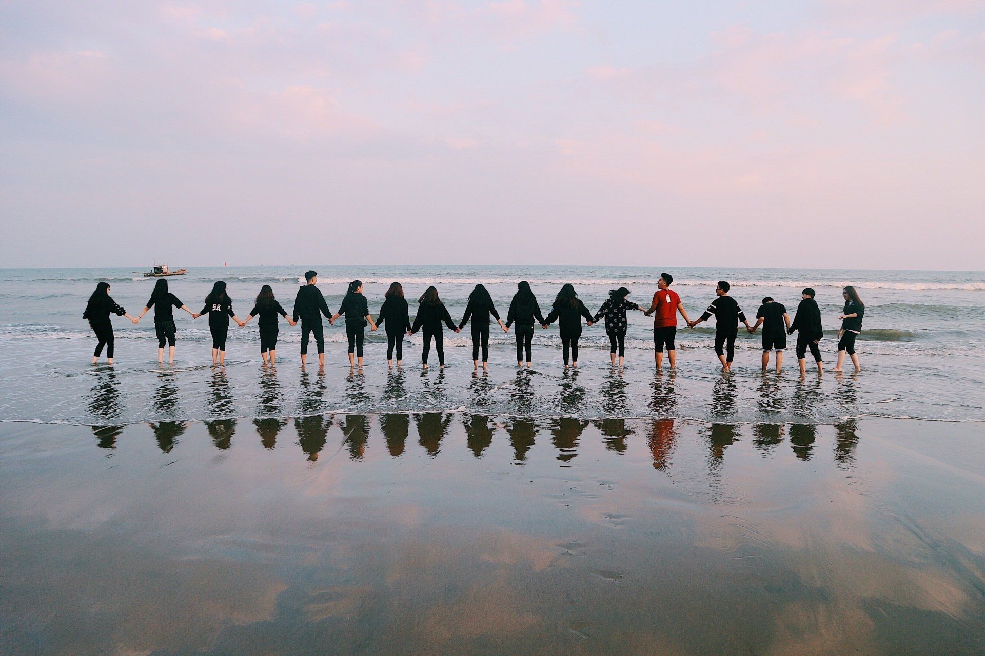 A group of people are standing on a beach holding hands.