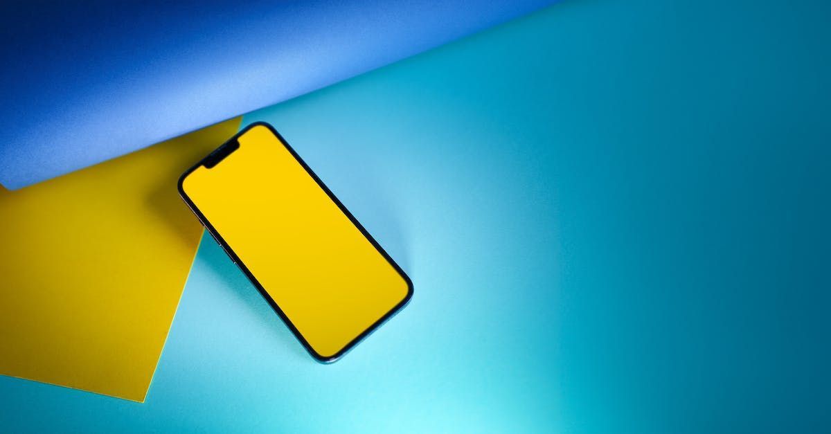 A cell phone with a yellow screen is sitting on a blue and yellow surface.