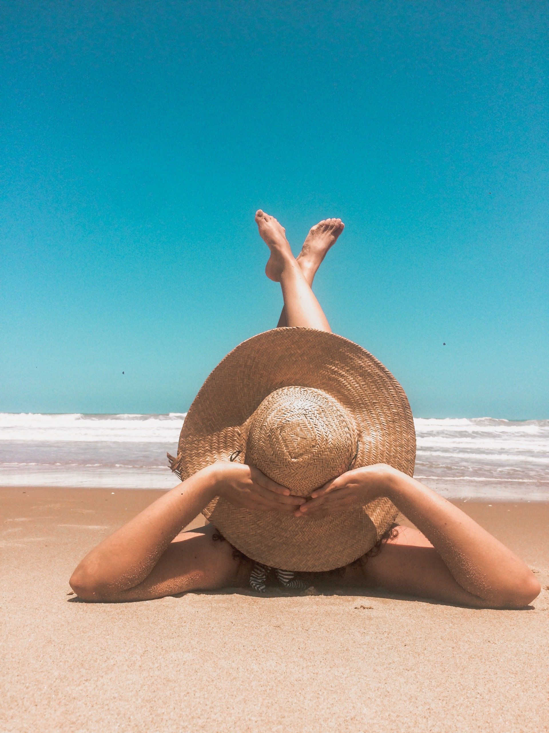 A woman is laying on the beach wearing a straw hat.