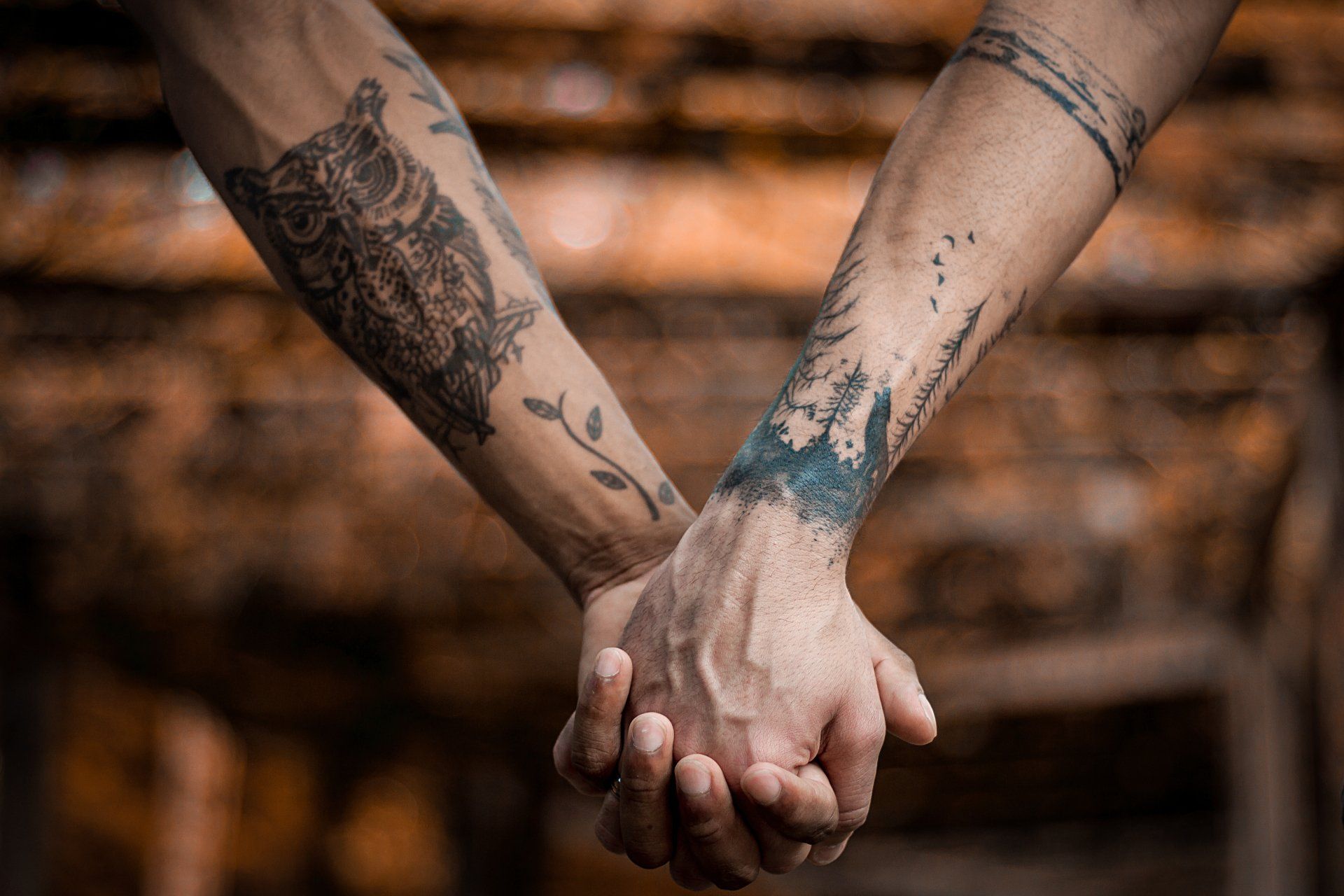 Two individuals are holding hands, both have tattoos, representing a relationship of some type