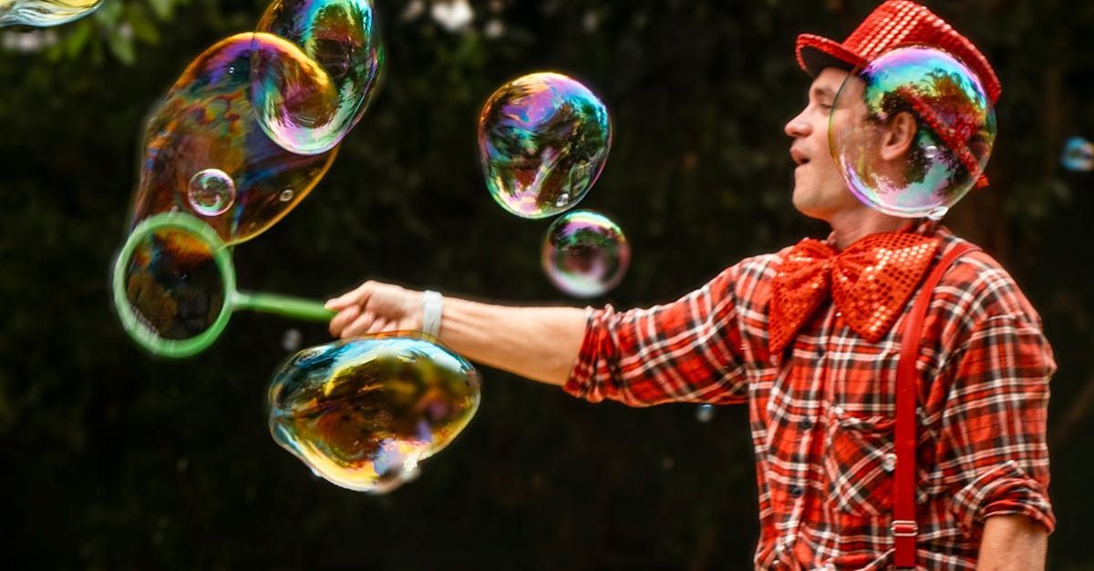 A clown is blowing soap bubbles in a park.