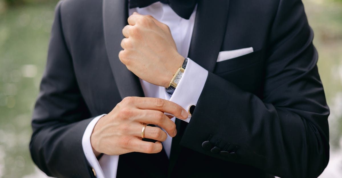 A man in a tuxedo is fixing his cufflinks.