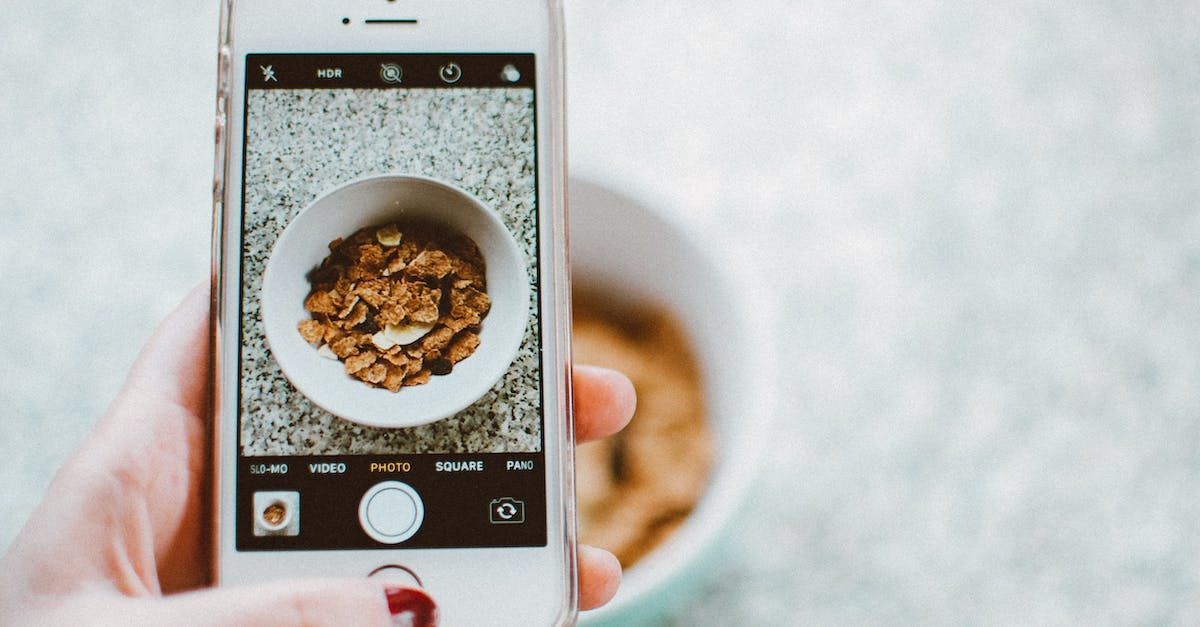 A person is taking a picture of a bowl of cereal with a cell phone.