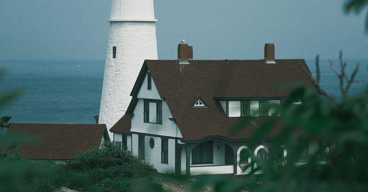 A house with a lighthouse in the background and the ocean in the background.