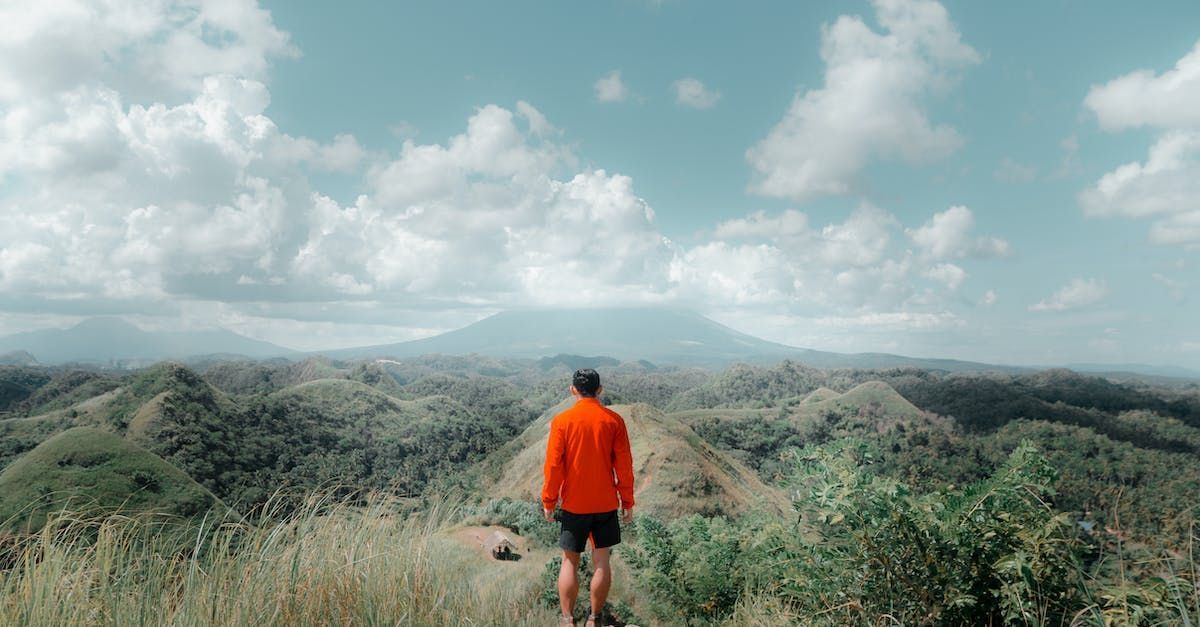 A man in an orange jacket is standing on top of a mountain.