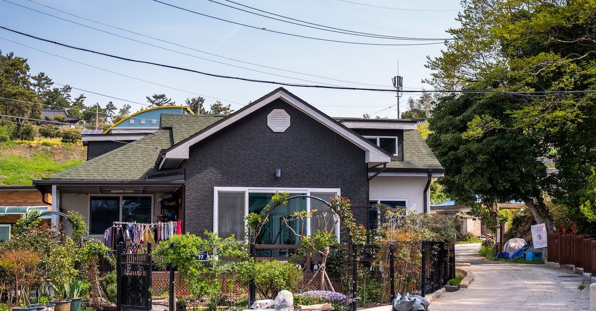 House with gray and white exterior, garden in front, and trees.