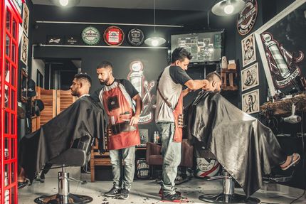 Two barbers in a shop working on customers