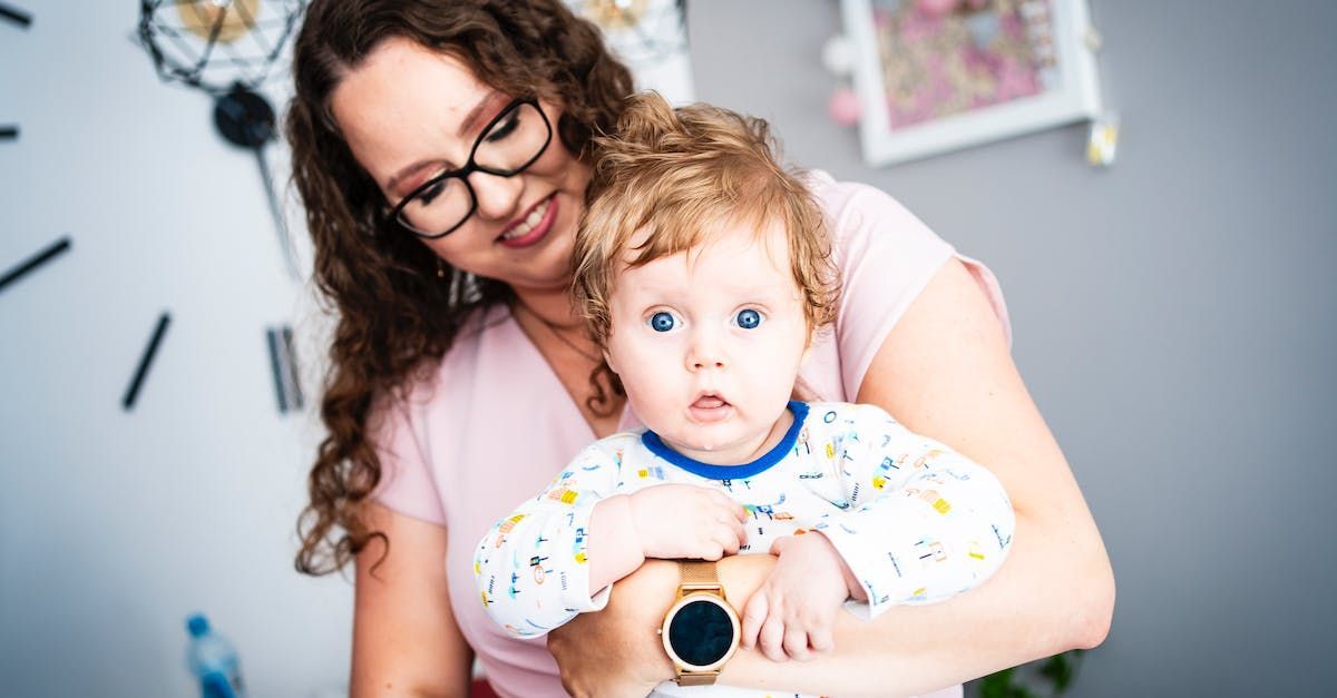 A woman is holding a baby in her arms while wearing a smart watch.