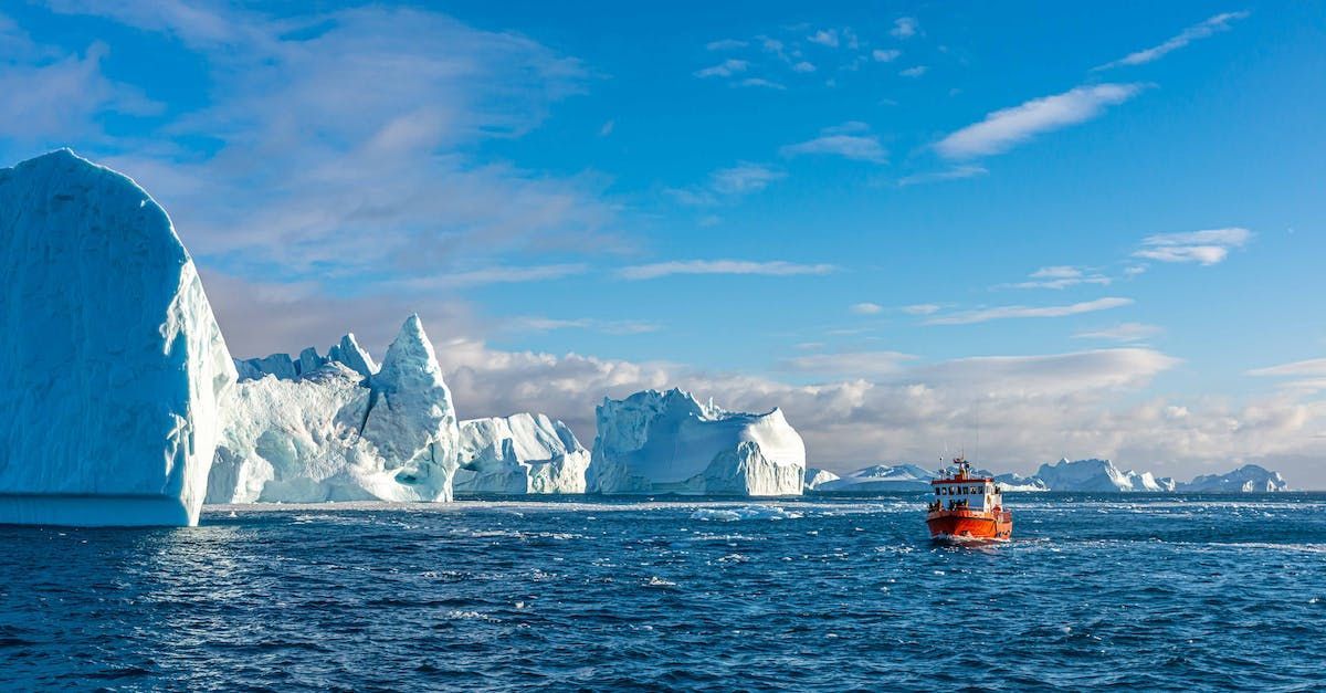 A boat is floating in the greenland ocean with icebergs in the background.