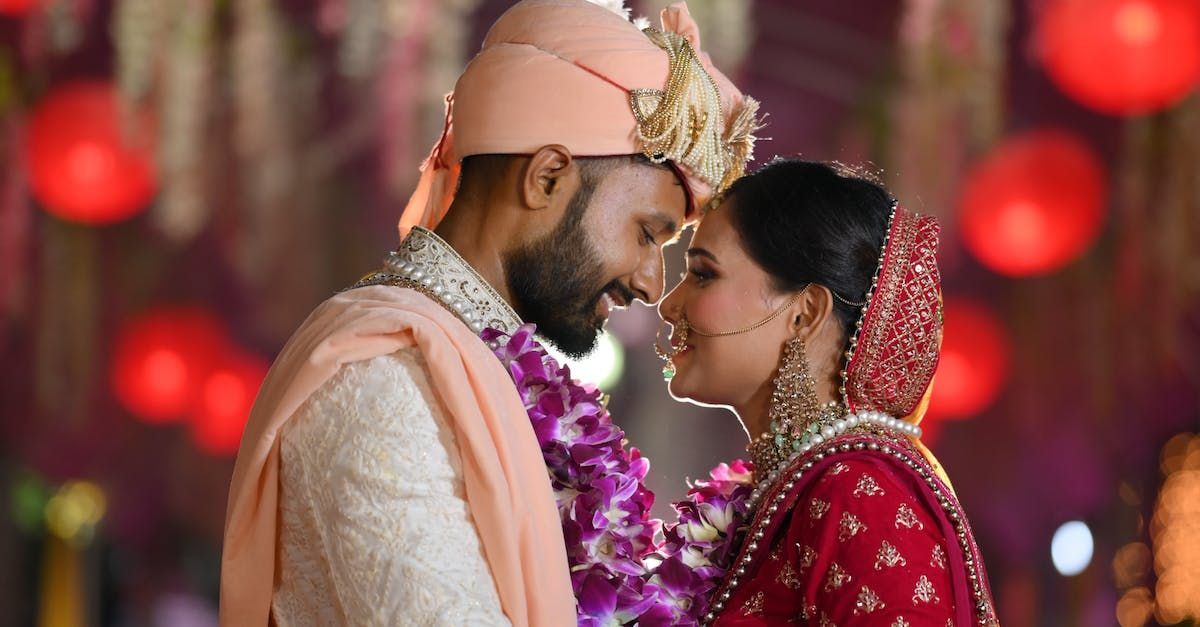 Indian wedding couple, man in peach turban and embroidered cream suit, woman in red sari, 