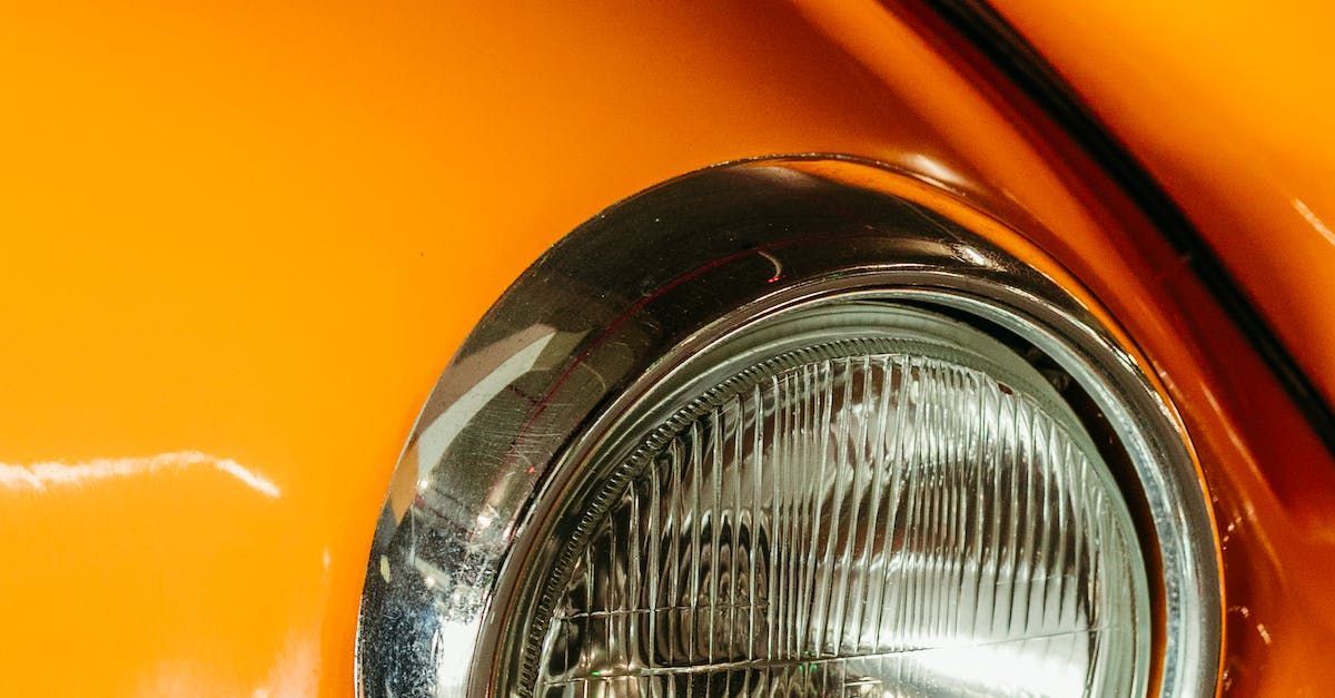 Close up of a car headlight. The headlight is ringed with silver and the vehicle is a clementine-orange colour.