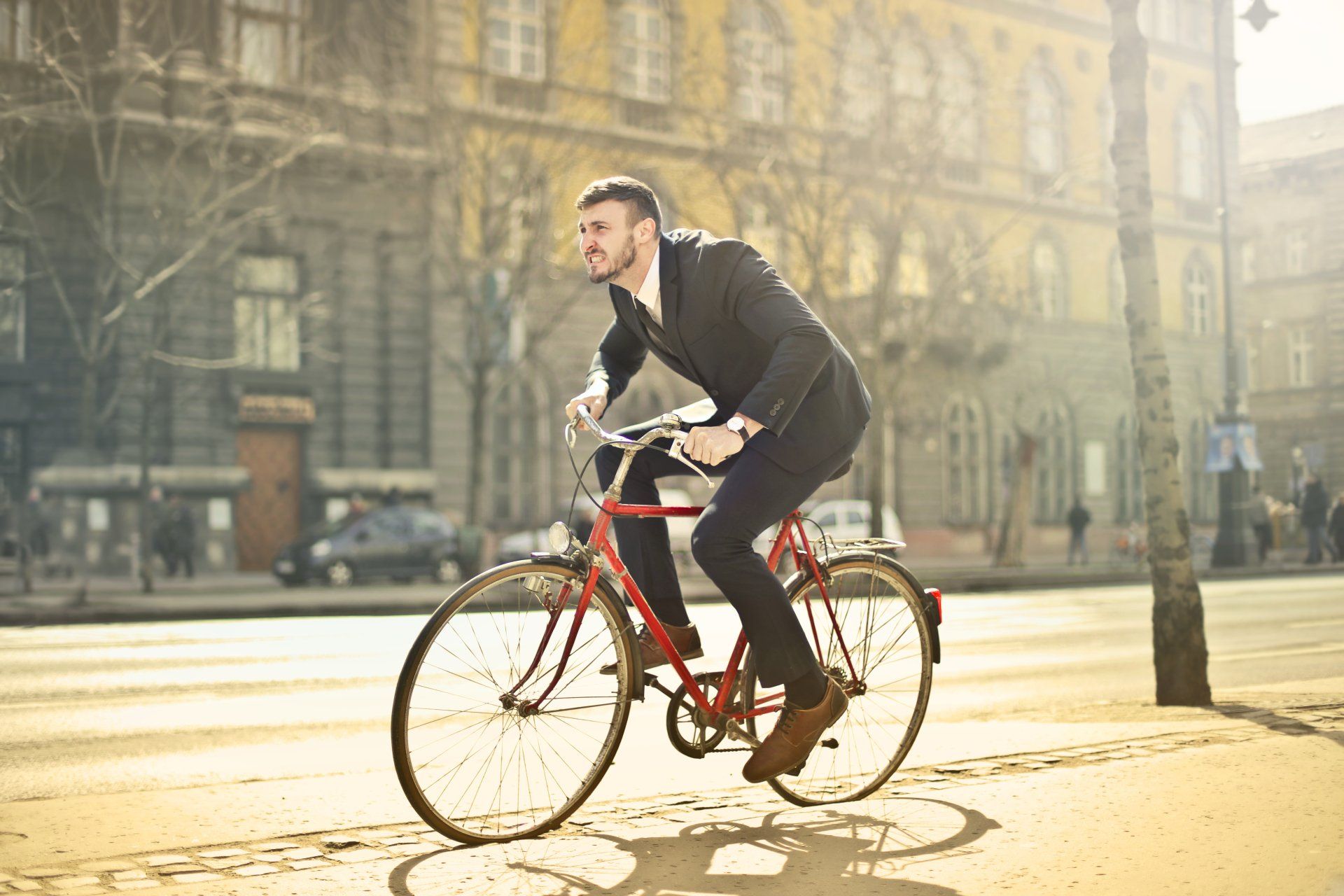 A man in a suit is riding a red bicycle down a city street.