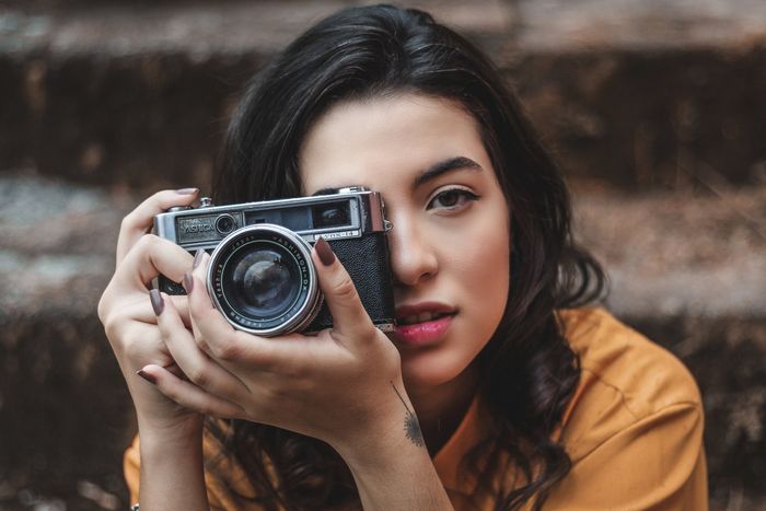 A woman is holding a camera in front of her face.