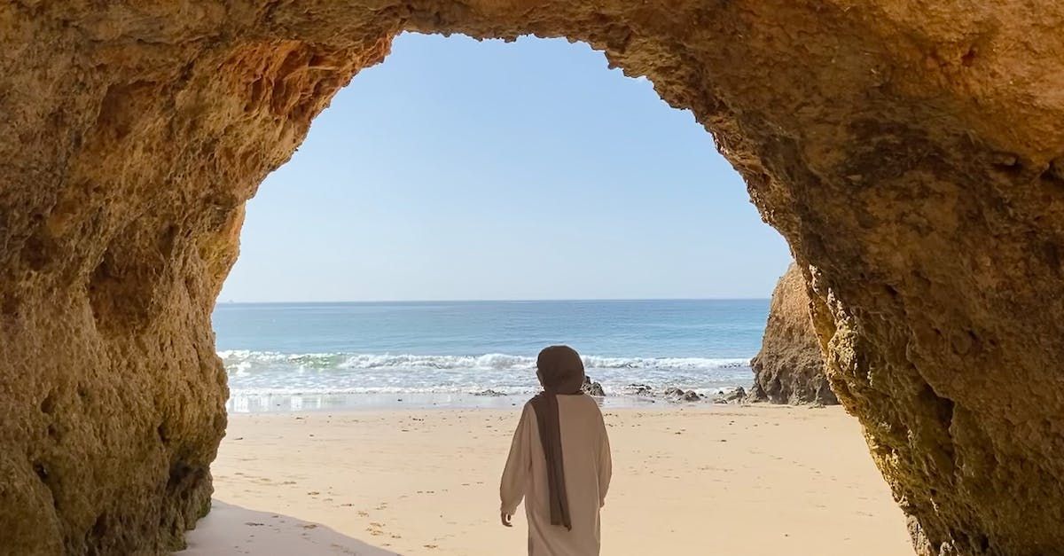 Woman in Headscarf Walking on a Sand Beach Under a Rock Arch in Alvor, Algarve Portugal - The Algarve Holidays Barter's Travelnet