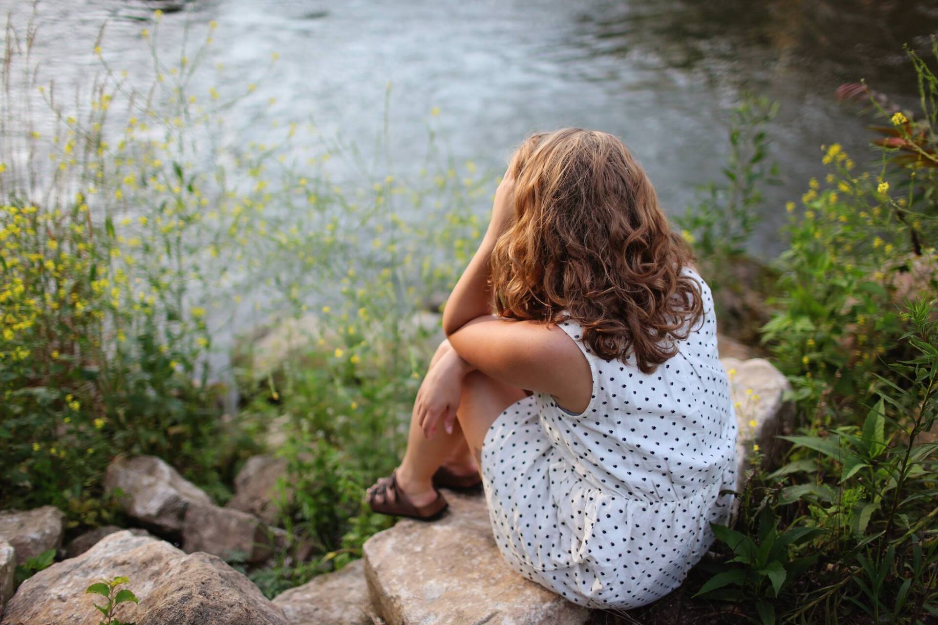 a young girl is sitting on a rock near a river 