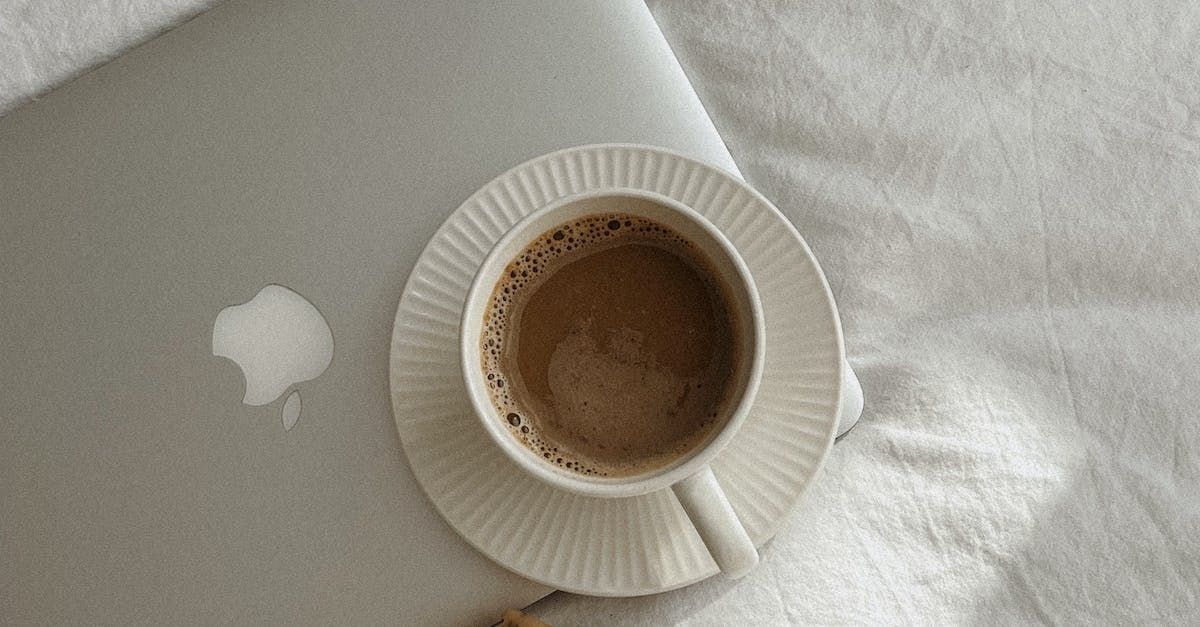 A cup of coffee is sitting on a saucer next to a laptop on a bed.