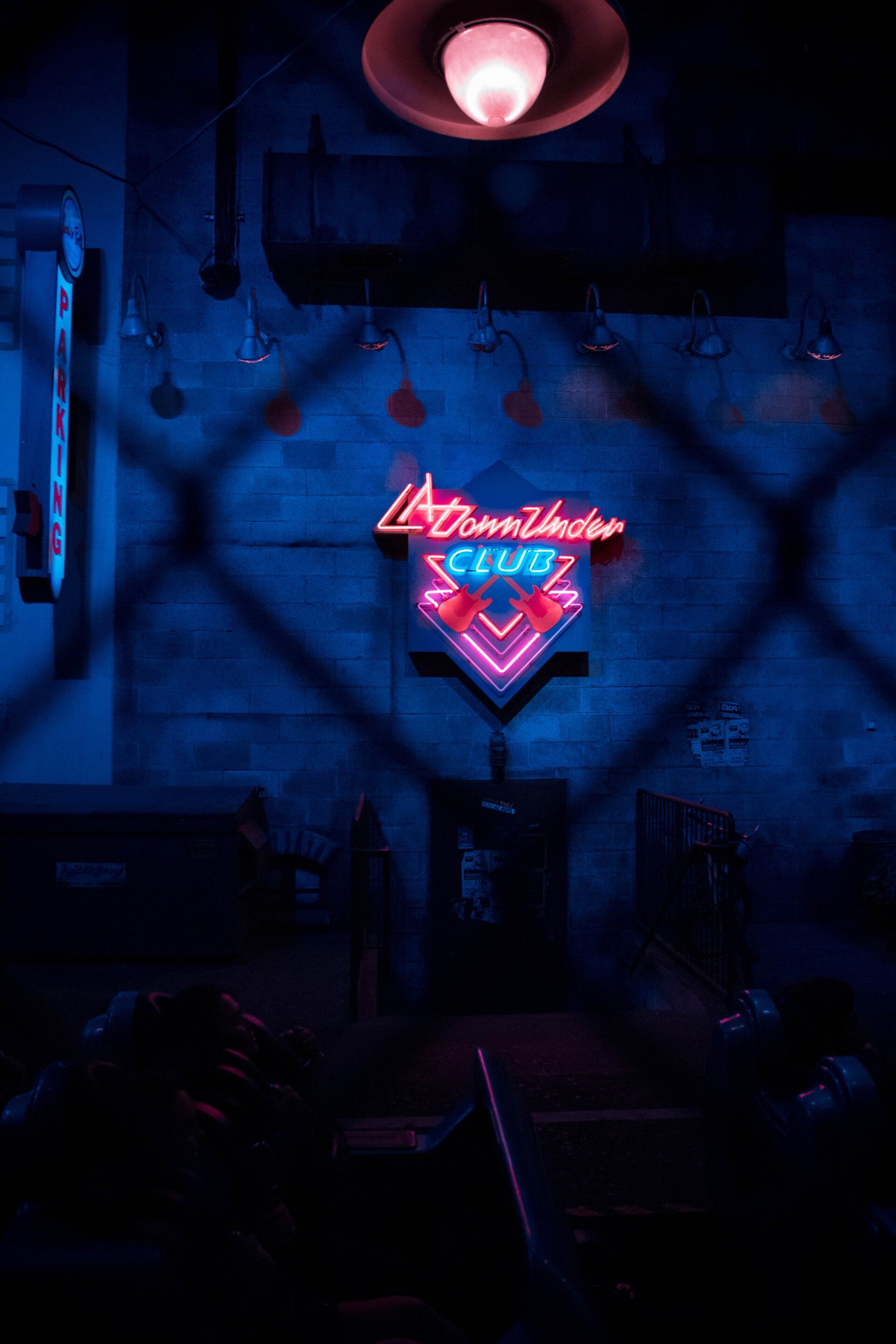A neon sign is behind a chain link fence in a dark room.