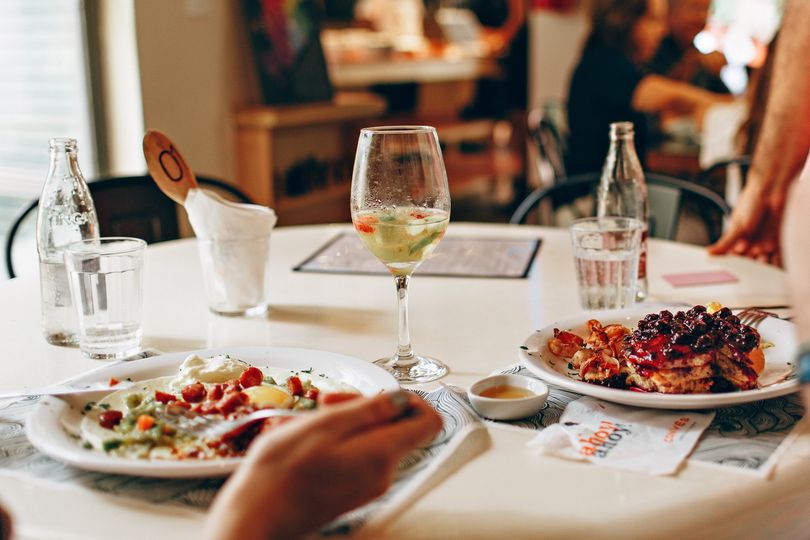 A person is sitting at a table with plates of food and a glass of wine.