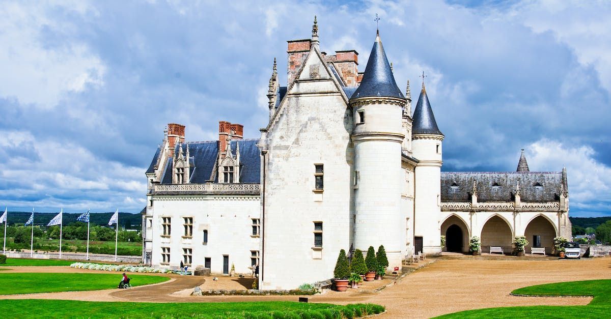 A large white castle with a blue roof is surrounded by green grass.