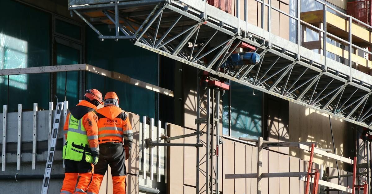 Two construction workers are standing in front of a building under construction.