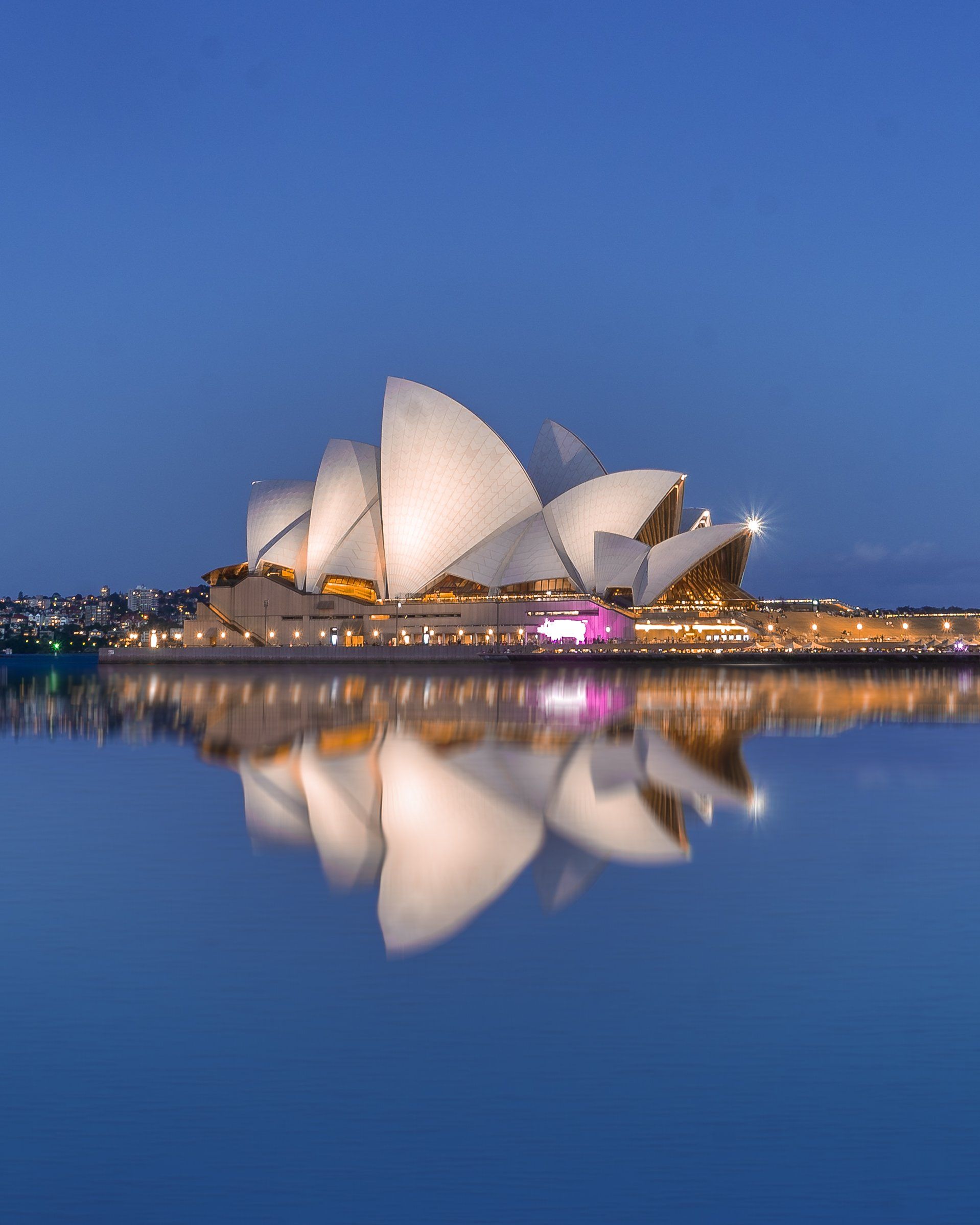 The sydney opera house is reflected in the water at night